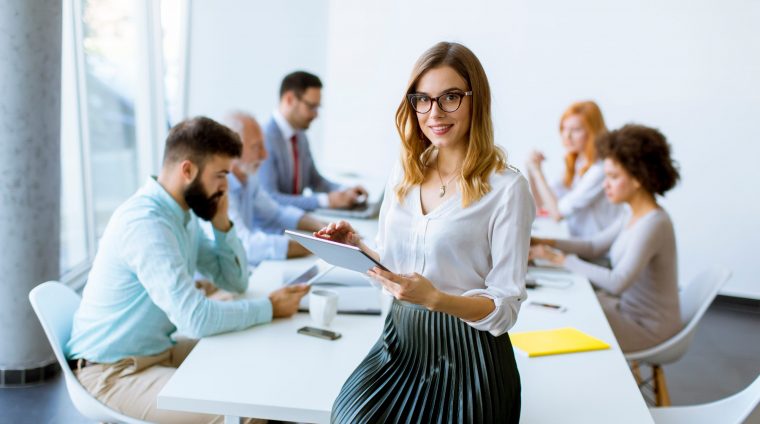 Young attractive female manager working on digital tablet while standing in modern office